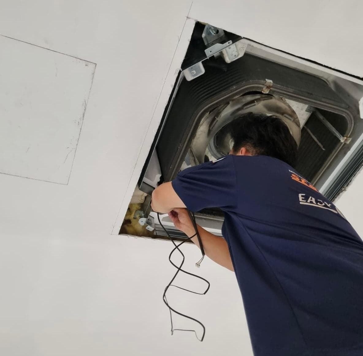 Technician working inside a ceiling cassette aircon with the front panel removed