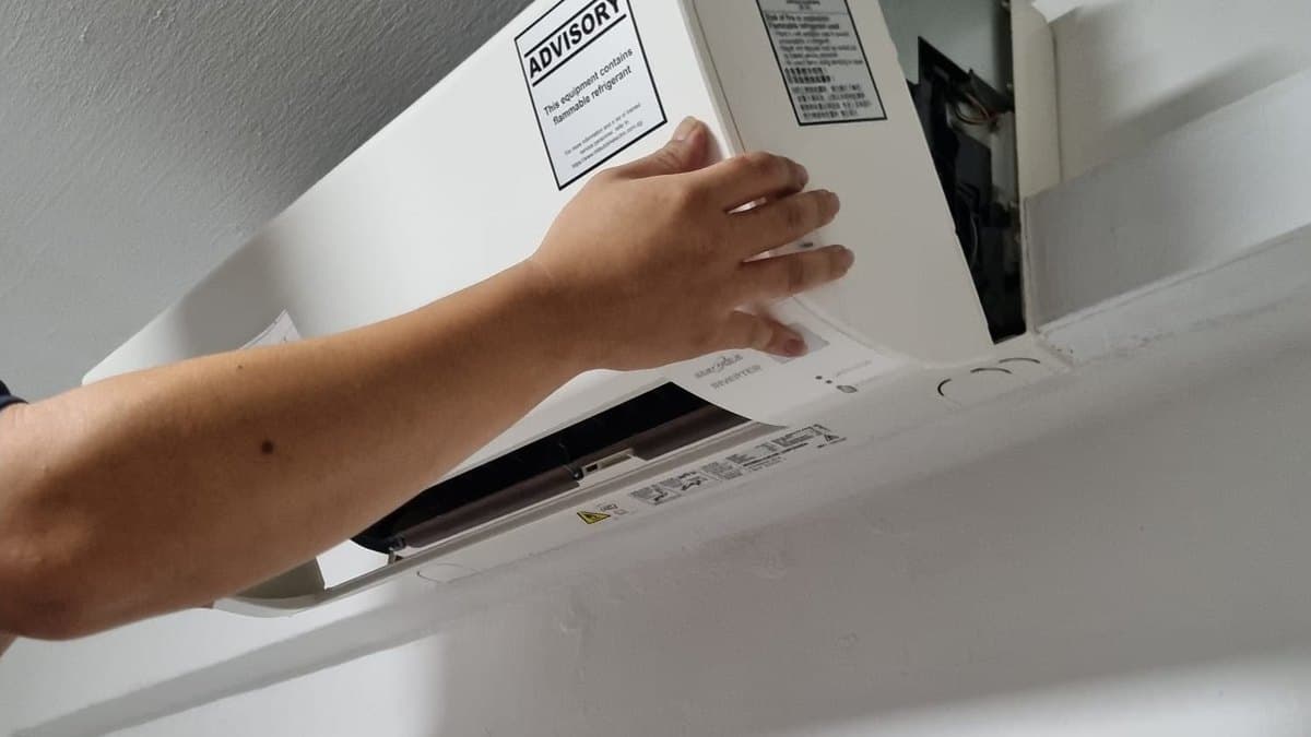 Technician refitting the front cover of the aircon after servicing