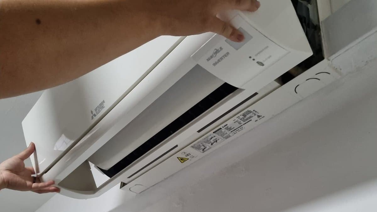 Technician opening the front cover of a wall-mounted aircon before servicing
