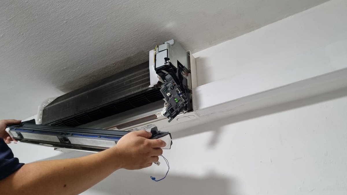Technician sliding the air filter out of an aircon indoor unit