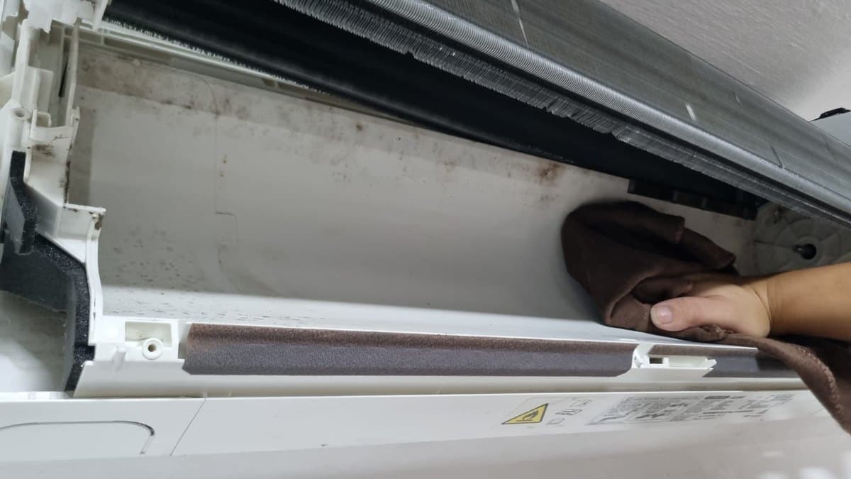 Mould and grime being wiped out of the drainage tray under an aircon cooling coil